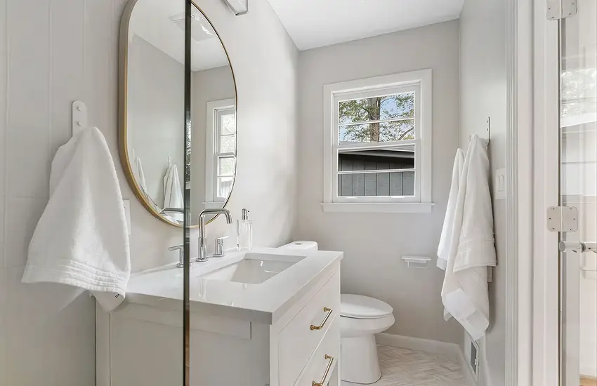 Remodeled bathroom with round mirror, white vanity, and glass shower