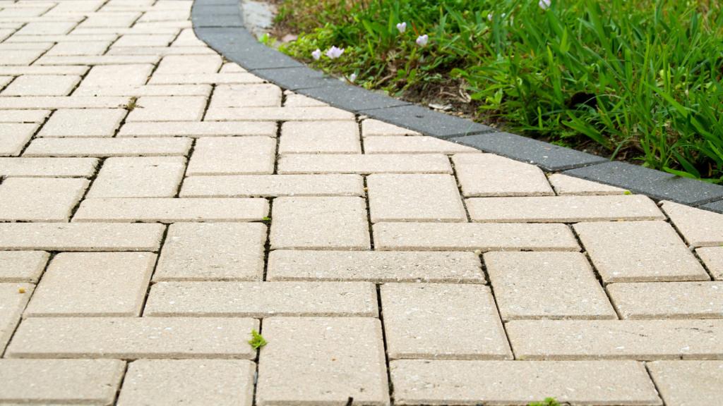 Pavers and hardscape walkway featuring light-colored rectangular pavers arranged in a staggered pattern beside landscaped greenery.