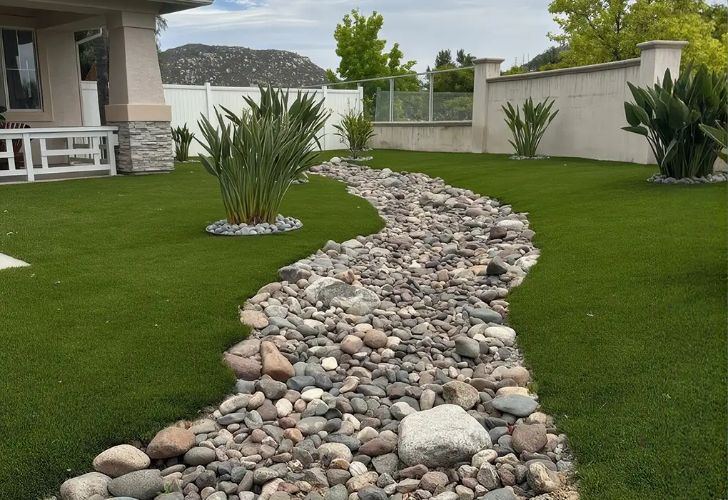 Original photo of an artificial turf lawn with a curving river-rock dry creek bed and bird-of-paradise planting islands